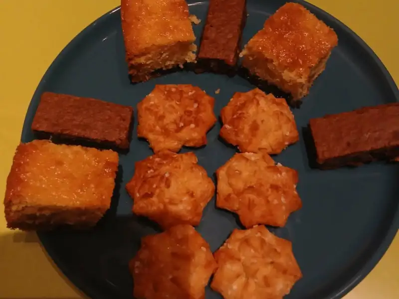 Teller mit selbstgemachten Leckereien: goldbraune Rührkuchen-Quadrate, Brownie-Stäbchen und Butterplätzchen mit Hagelzucker auf einem blauen Teller