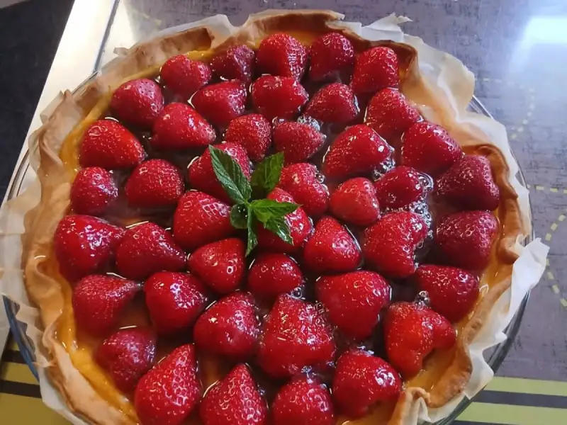 Selbstgemachte glasierte Erdbeertarte, ganze Erdbeeren auf Vanillecreme, mit Minze dekoriert, in einer Glasform