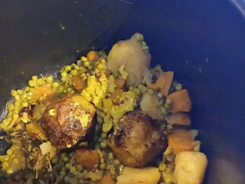 Fleischbällchen mit Erbsen, Karotten und Kartoffeln mit Kurkuma, geschmort in einem schwarzen Schmortopf