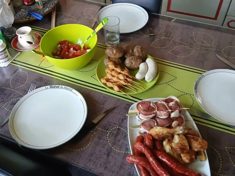 Rohe Hähnchenspieße auf einem Grilltisch mit Würstchen, Hähnchenunterschenkeln, Speckröllchen und Tomatensalat