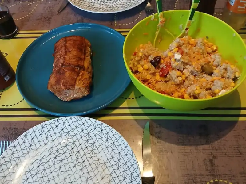 Goldbraun gebackener Lachsbraten auf einem blauen Teller neben einer Schüssel Reissalat mit Mais, Tomaten, Feta und Oliven