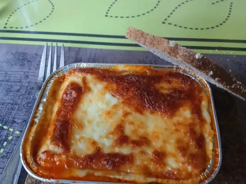 Selbstgemachte Lasagne-Portion: eine schön überbackene Aluschale mit einer Scheibe geröstetem Brot