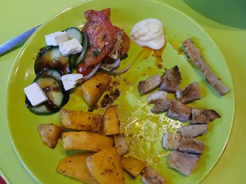 Teller mit gegrillten Schweinekotelett-Stücken, Ofenkartoffeln und griechischem Salat mit Gurke, Tomaten und Feta
