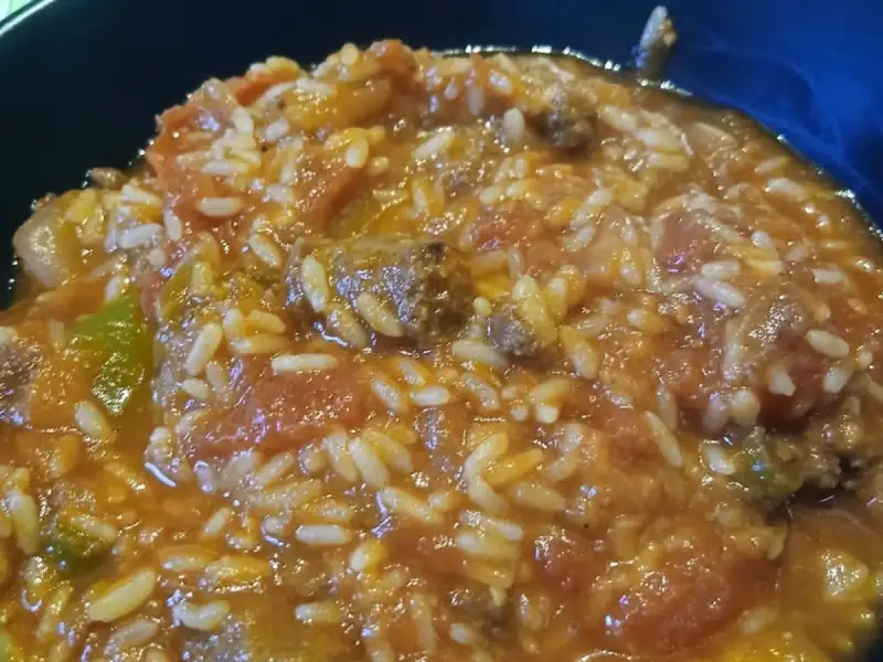 Tiefer Teller mit geschmortem Tomatenreis, Rindfleischstücken und Paprika
