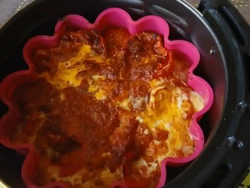 Überbackener Tomaten-Clafoutis mit Käse in einer rosa Silikonform im Korb eines Airfryers