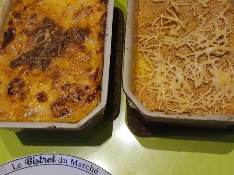 Goldbraun überbackener Lauch und selbstgemachtes Püree mit Semmelbröselkruste in zwei Auflaufformen auf einem grünen Tisch
